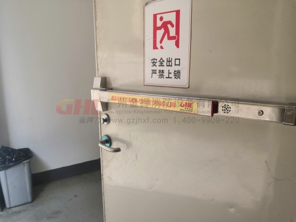 逃生門鎖警示標識，與錚亮的不銹鋼鎖體形成強烈對比